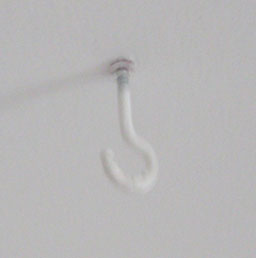 A white hook suspended from a white ceiling.